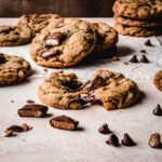 Melted chocolate spilling out of a Heath bar cookie broken in half next to scattered Heath pieces and chocolate chips.