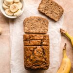 A loaf of banana bread with slices cut away and laying in front and a few more slices cut into the loaf.
