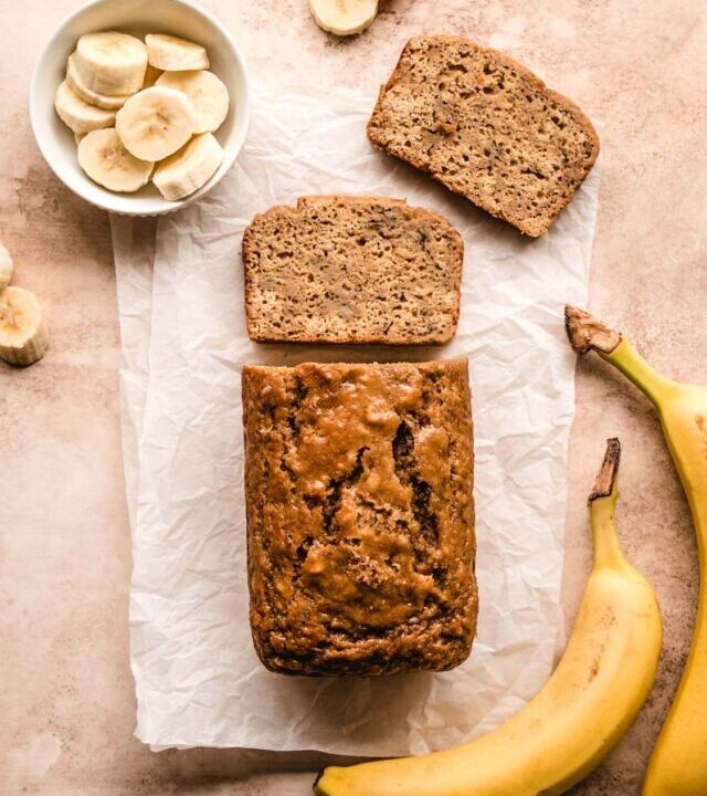 Top view of a loaf of banana bread without baking soda with two bananas beside it and a couple of slices laying in front of the loaf.