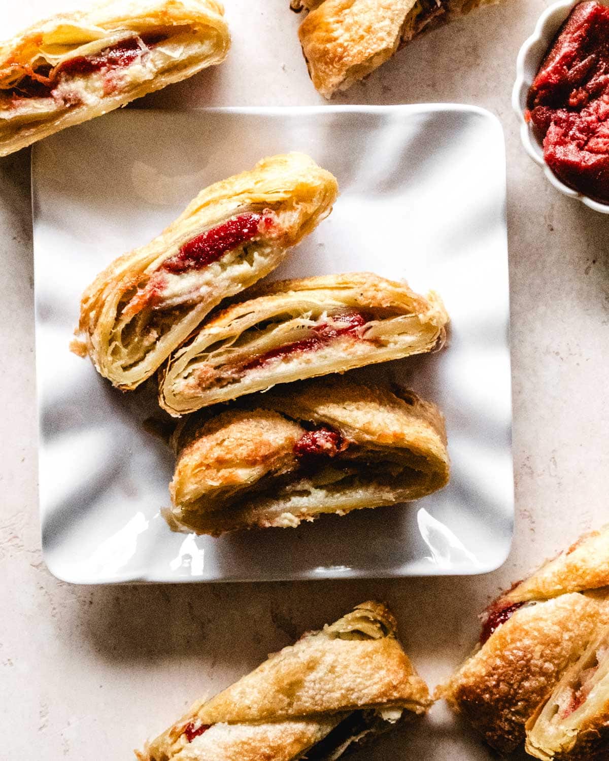Three slices of puff pastry filled with cream cheese and guava on a white plate.